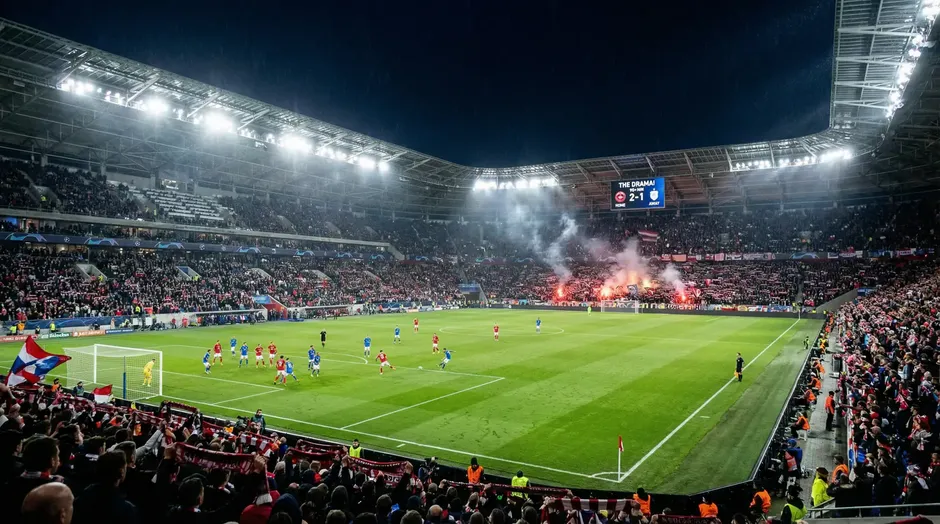 Oplyst fodboldstadion fyldt med tilskuere under en VM-aftenkamp med dramatisk belysning